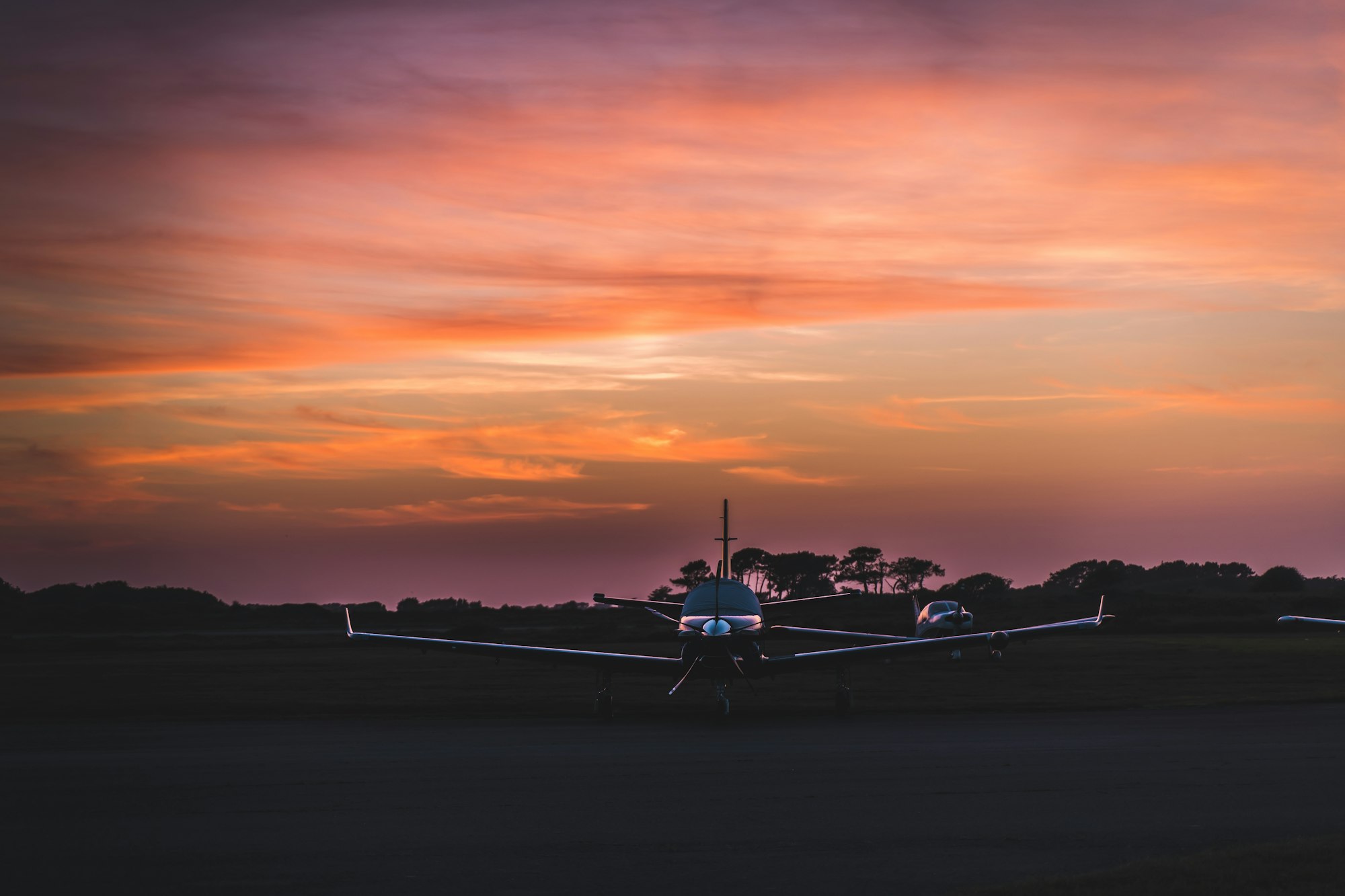A single-engine training airplane parked on the grass in front of a hangar.