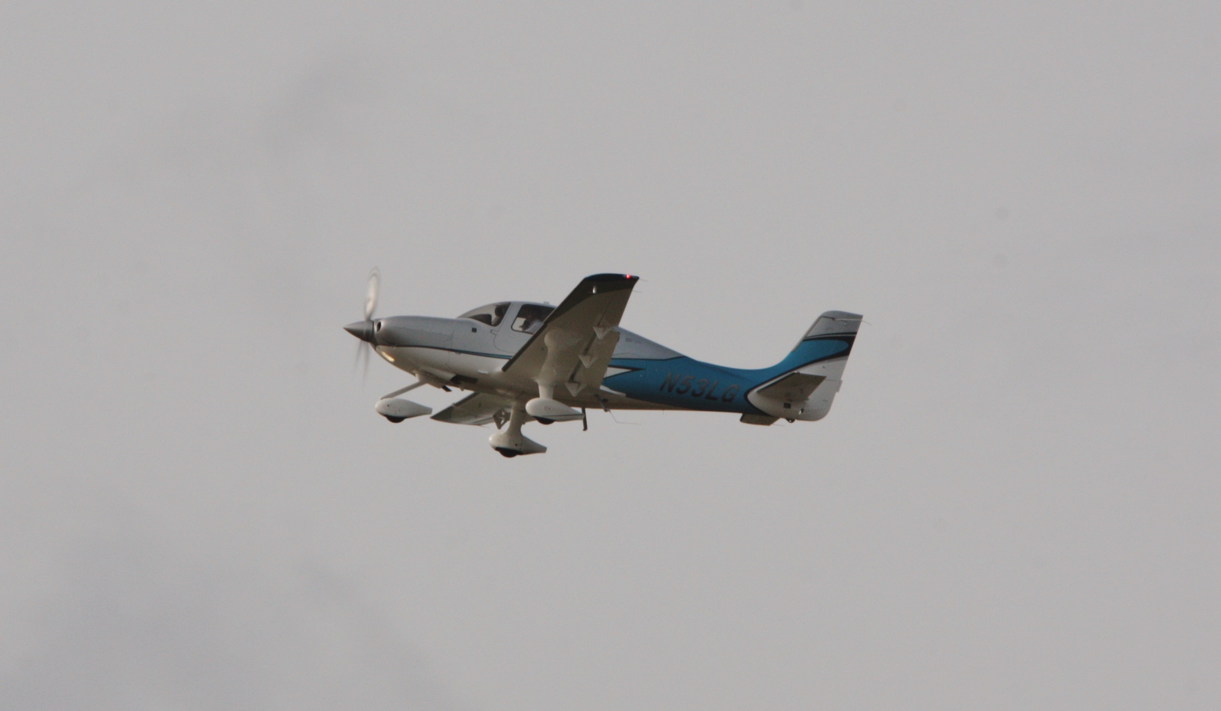 A Cirrus SR22T on approach, gear down, against a soft grey sky